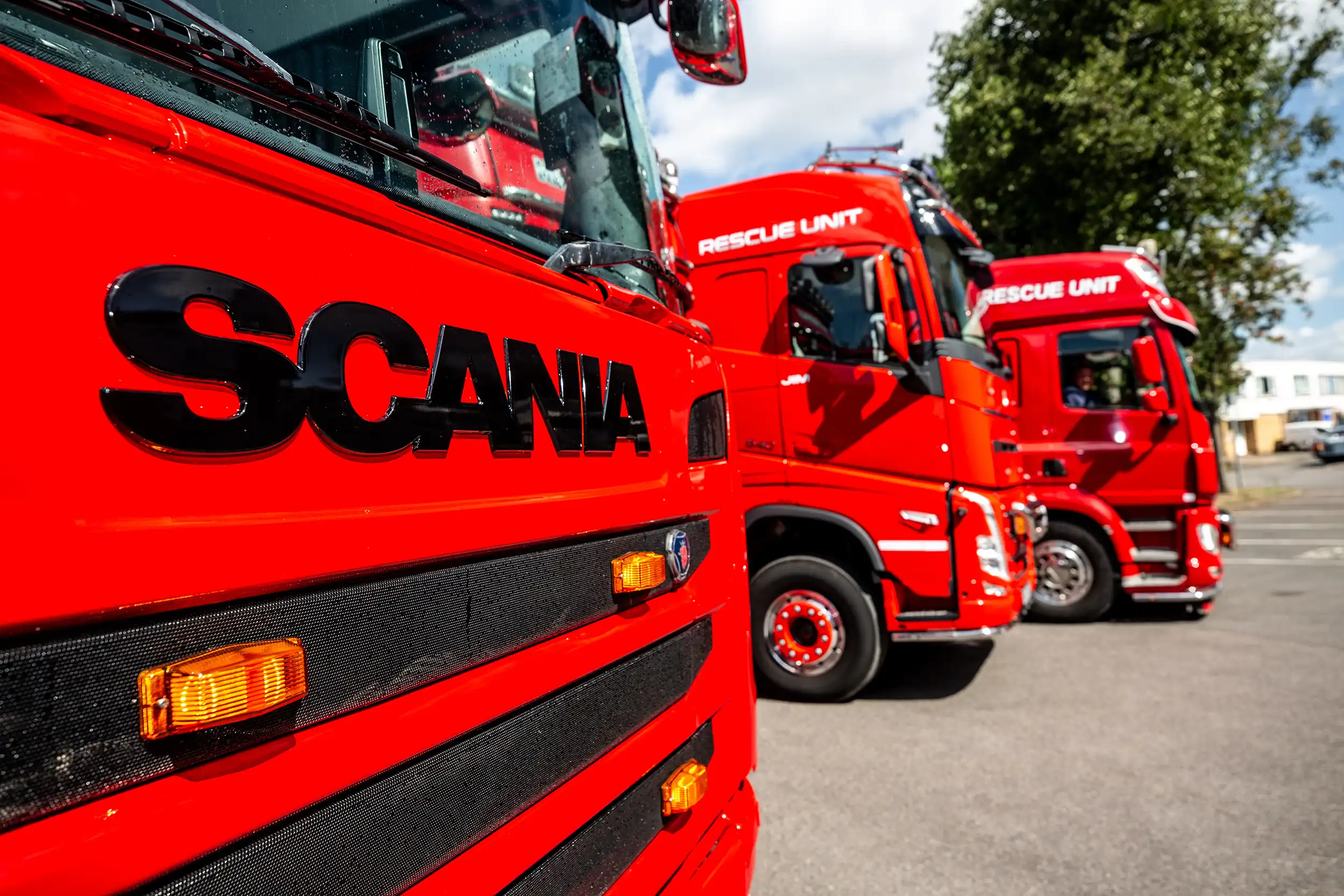Close-up of red Scania rescue unit trucks parked in a row outdoors on a sunny day.