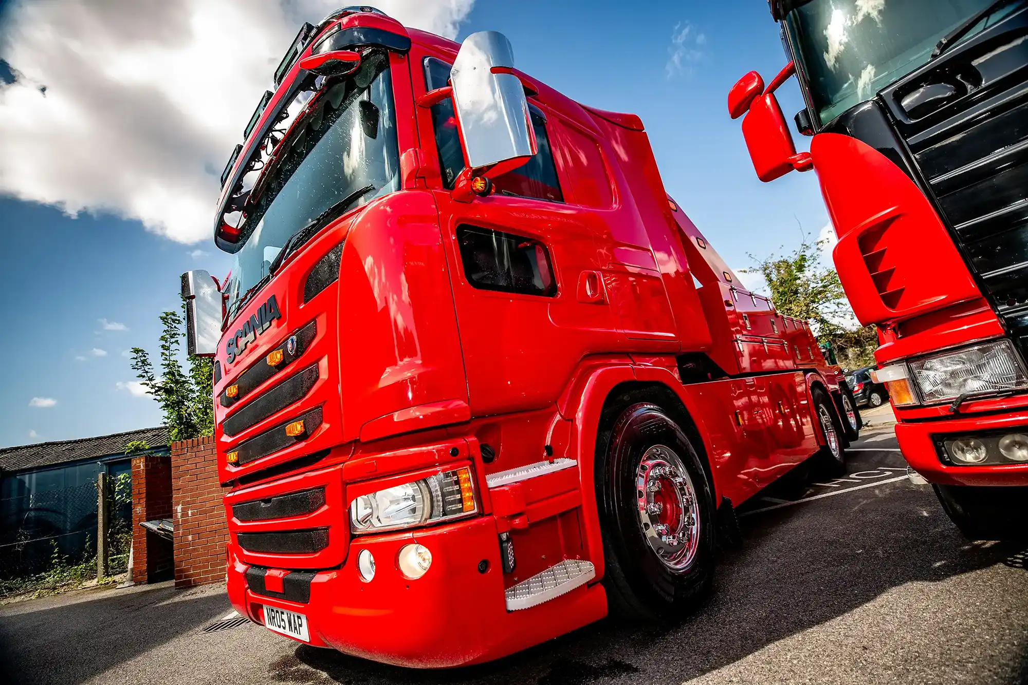 Bright red Scania heavy-duty truck with chrome wheel rims parked on a sunny day.