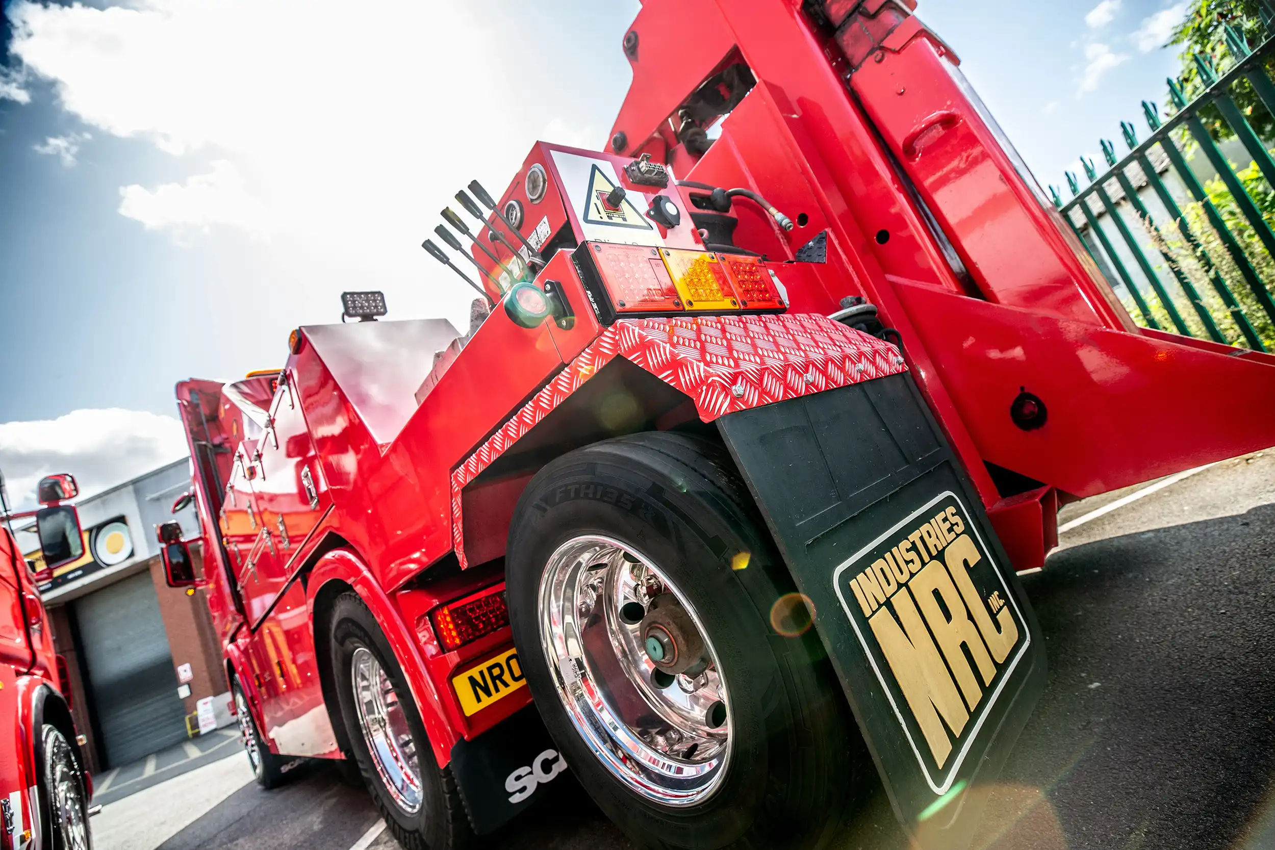 Low-angle side view of a red heavy-duty tow truck with shiny chrome wheels parked outdoors.