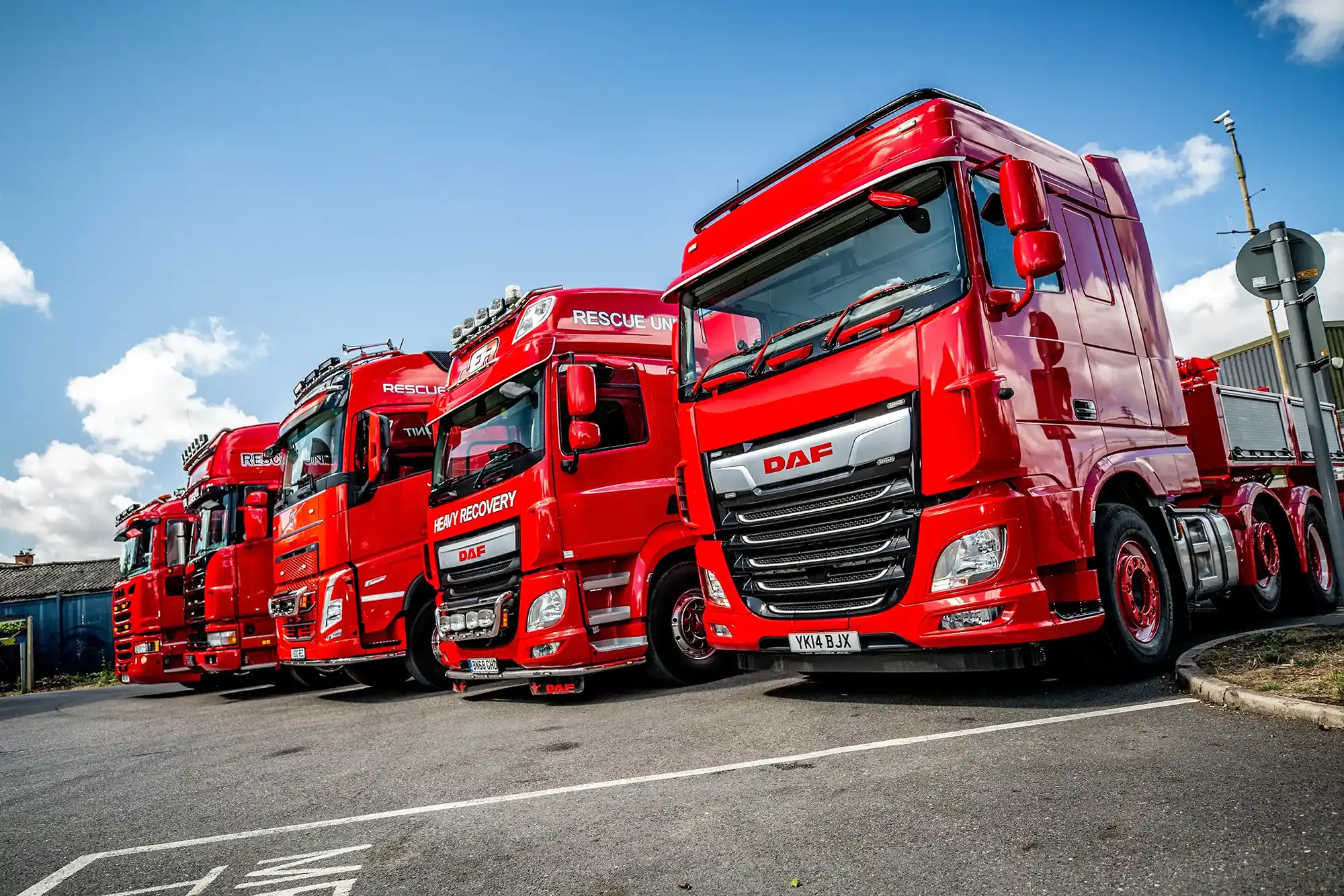Row of bright red heavy recovery trucks parked under a partly cloudy blue sky.