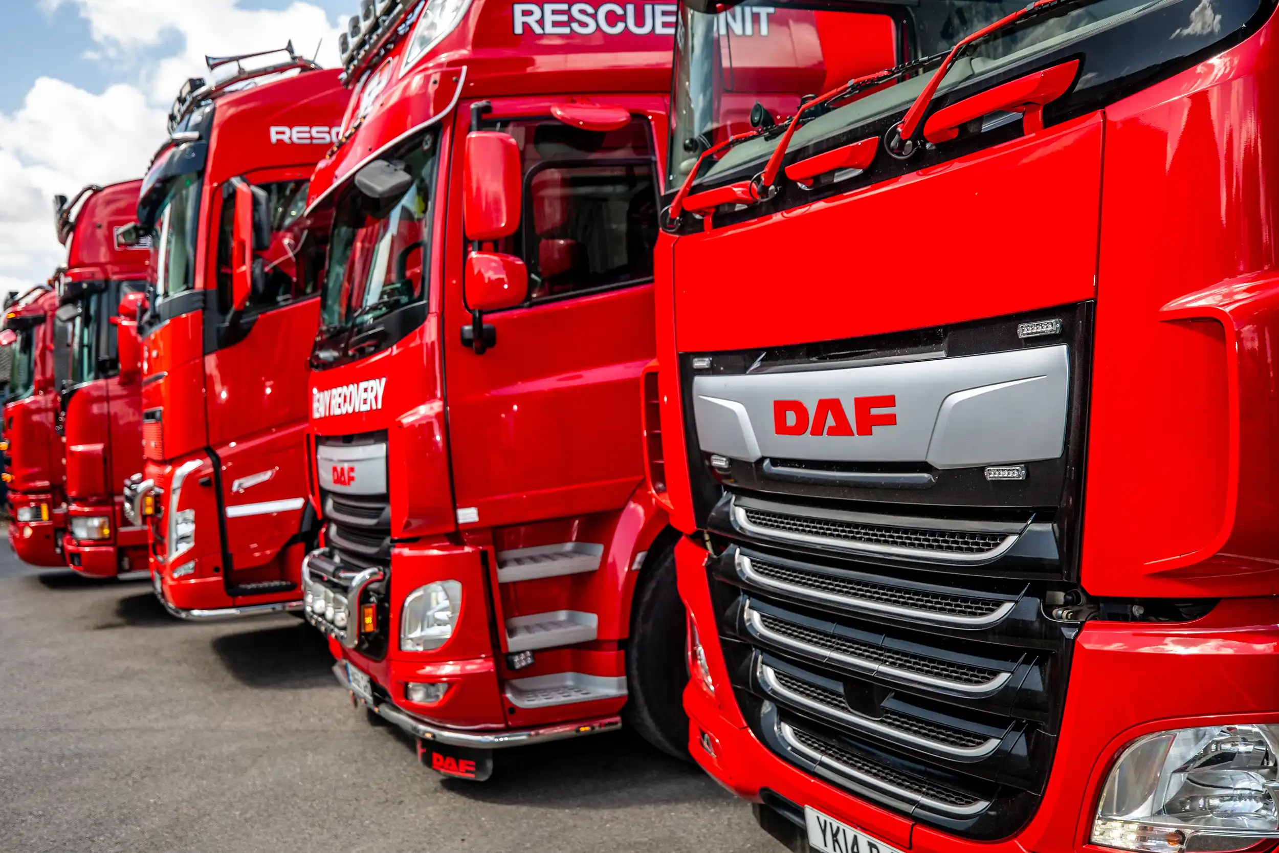 Row of red DAF rescue unit trucks parked on asphalt under a partly cloudy sky.