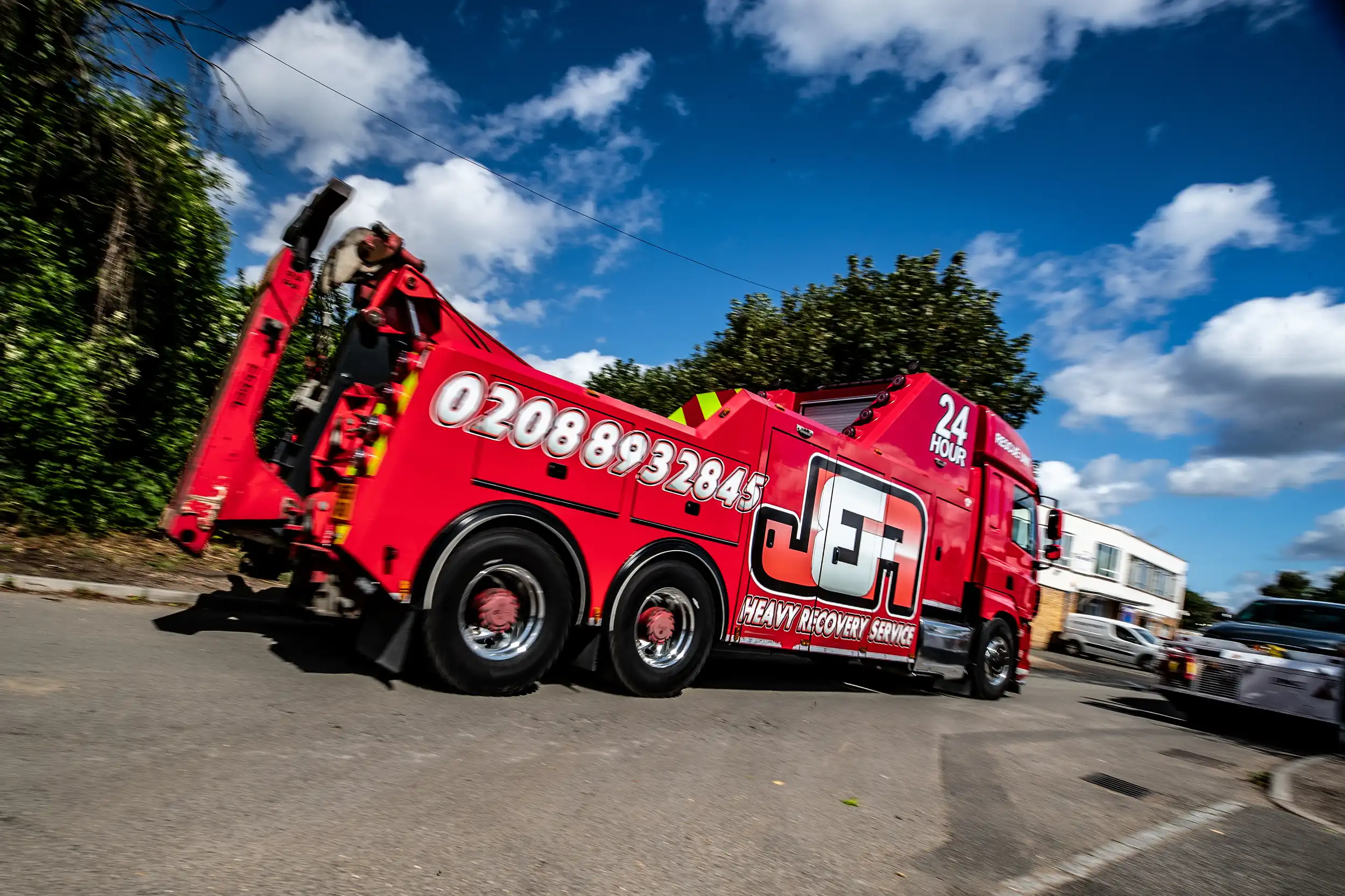 Red heavy recovery truck with phone number 02088932845 and JEA 24 hour service logo on side.