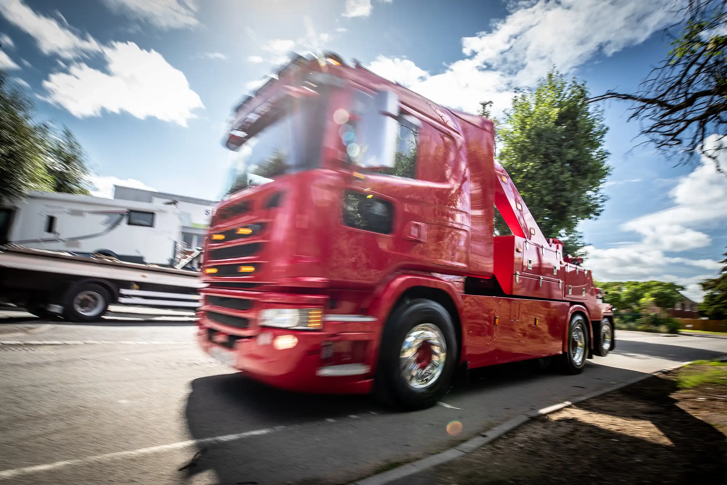 Red tow truck driving on a sunny street with motion blur and blue sky with clouds.