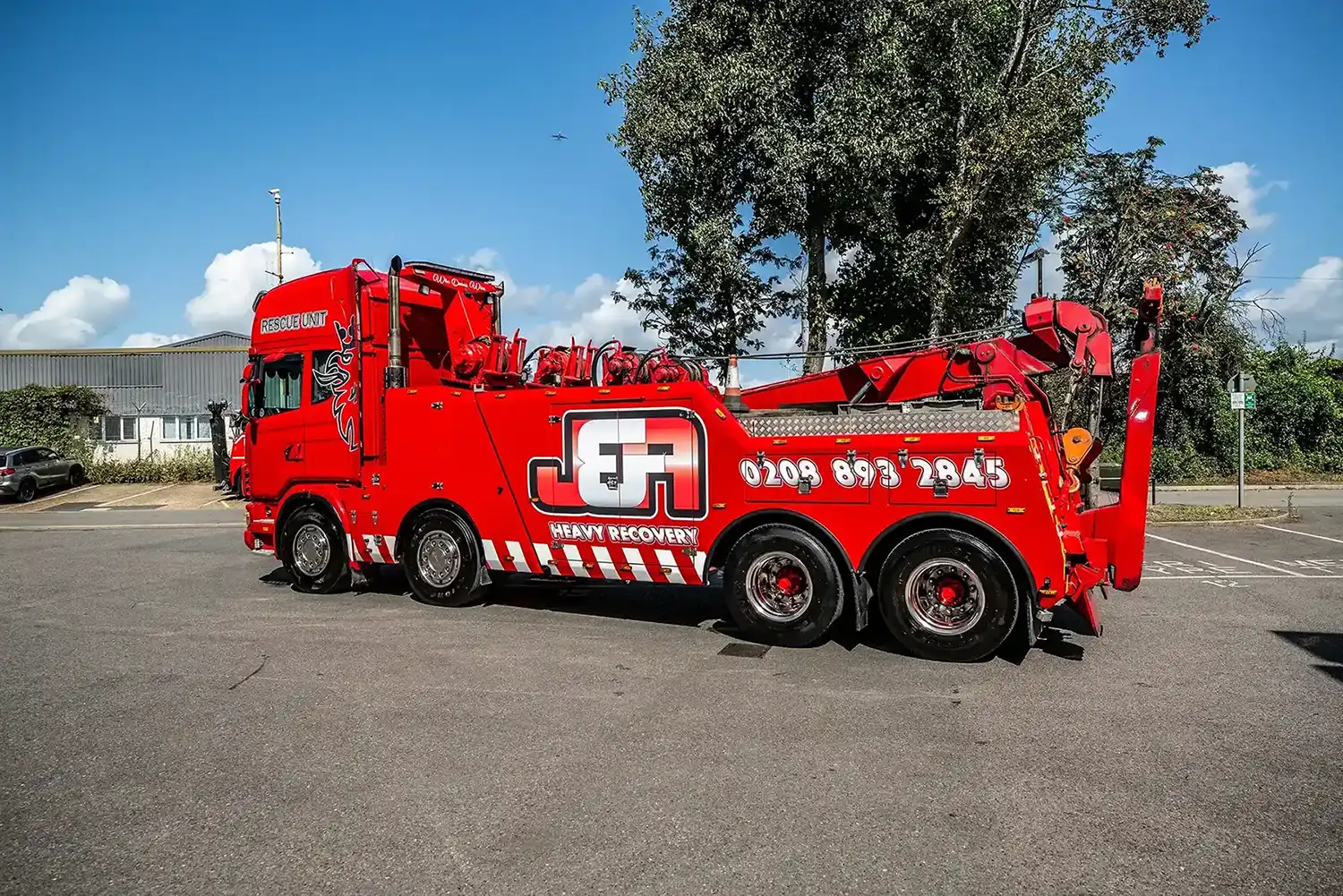 Bright red heavy recovery rescue truck with large towing equipment parked on road under blue sky.