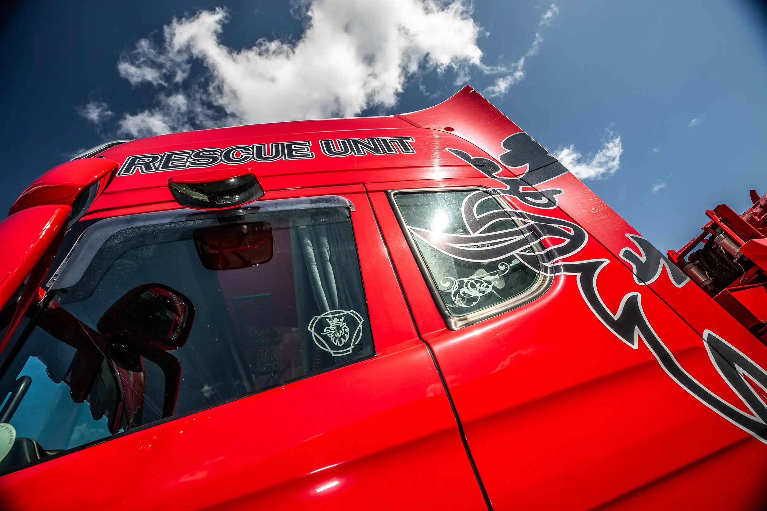 Red Rescue Unit vehicle cab with tribal-style black and white decals under a partly cloudy sky.