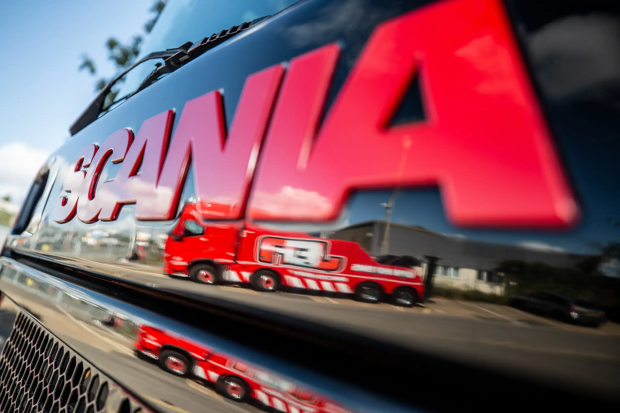 Reflection of a red truck on the shiny black surface with large red SCANIA text above it.