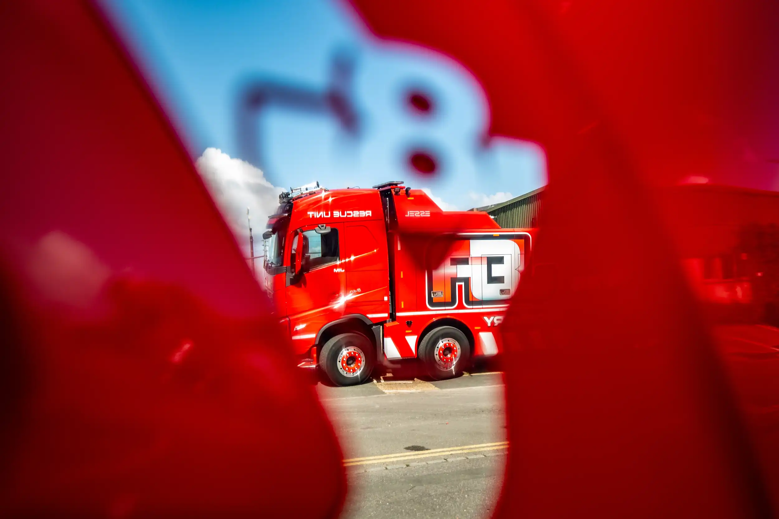 Red rescue unit truck seen through a cutout in a red barrier with a blue sky background.